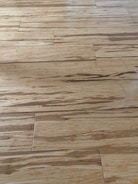 Wooden floor with a natural grain pattern and a light brown color. The surface appears smooth with slightly visible seams between the planks, giving it a polished look.