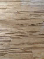 Wooden floor with a natural grain pattern and a light brown color. The surface appears smooth with slightly visible seams between the planks, giving it a polished look.