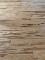 Wooden floor with a natural grain pattern and a light brown color. The surface appears smooth with slightly visible seams between the planks, giving it a polished look.