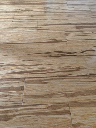 Wooden floor with a natural grain pattern and a light brown color. The surface appears smooth with slightly visible seams between the planks, giving it a polished look.
