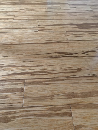 Wooden floor with a natural grain pattern and a light brown color. The surface appears smooth with slightly visible seams between the planks, giving it a polished look.