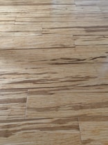 Wooden floor with a natural grain pattern and a light brown color. The surface appears smooth with slightly visible seams between the planks, giving it a polished look.