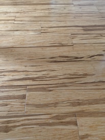 Wooden floor with a natural grain pattern and a light brown color. The surface appears smooth with slightly visible seams between the planks, giving it a polished look.