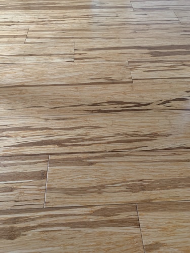 Wooden floor with a natural grain pattern and a light brown color. The surface appears smooth with slightly visible seams between the planks, giving it a polished look.