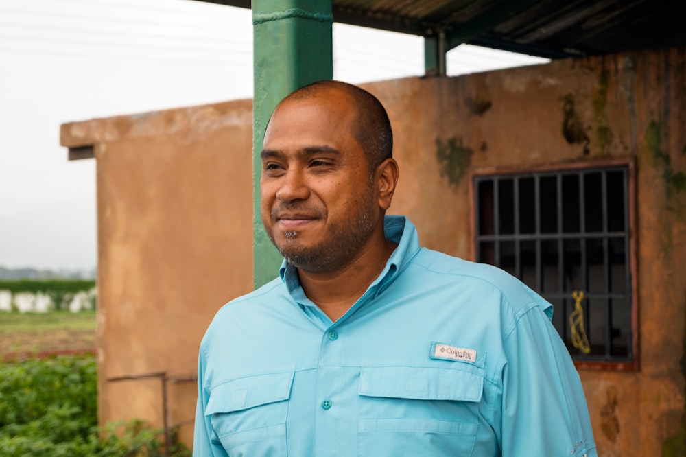 man in blue button up shirt standing near brown wall