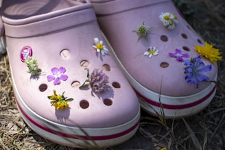 A vibrant pair of personalized Crocs adorned with colorful charms and glitter accents, set against a sunny outdoor backdrop.