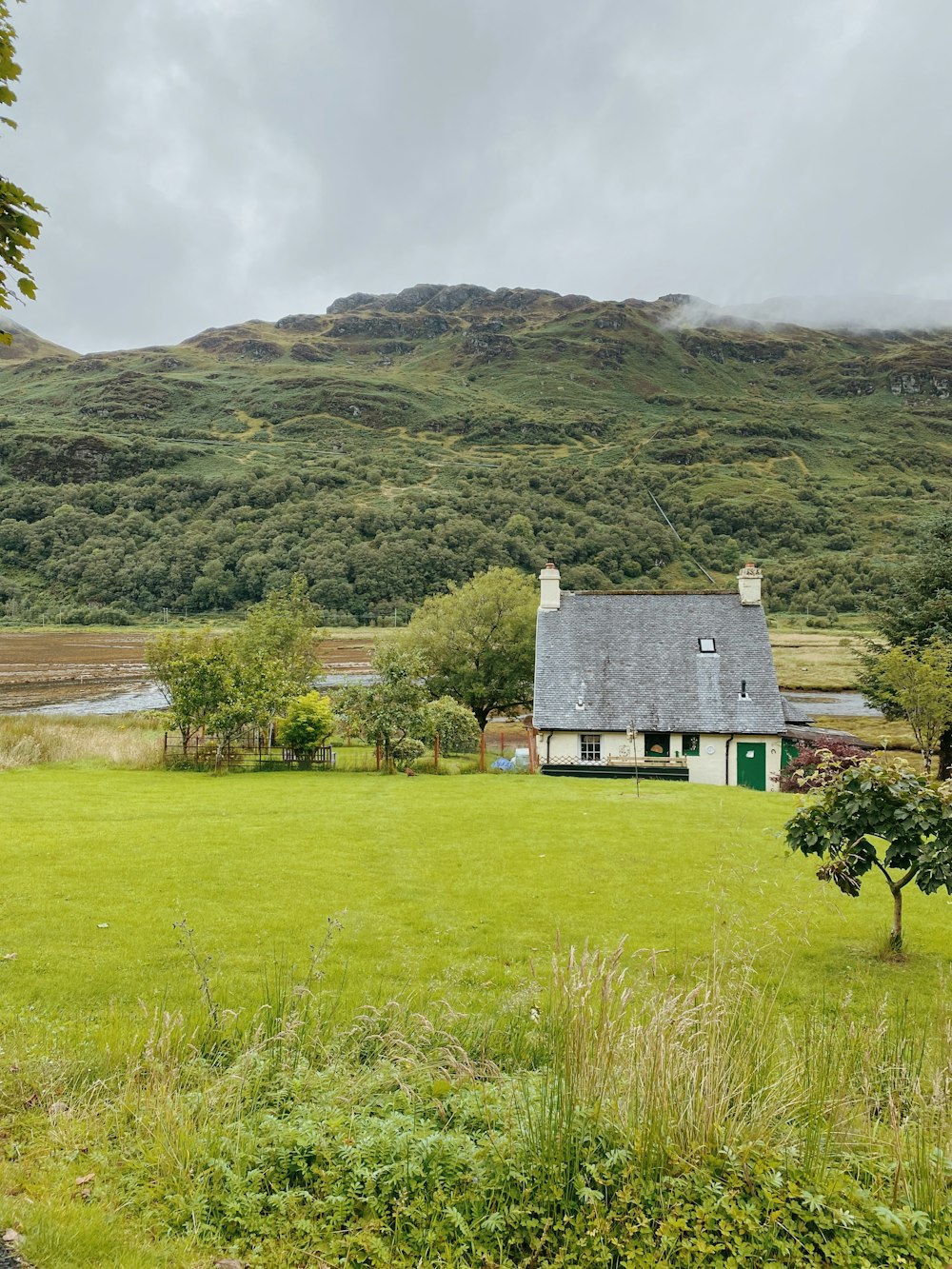 casa cinzenta e branca no campo de grama verde perto da montanha durante o dia