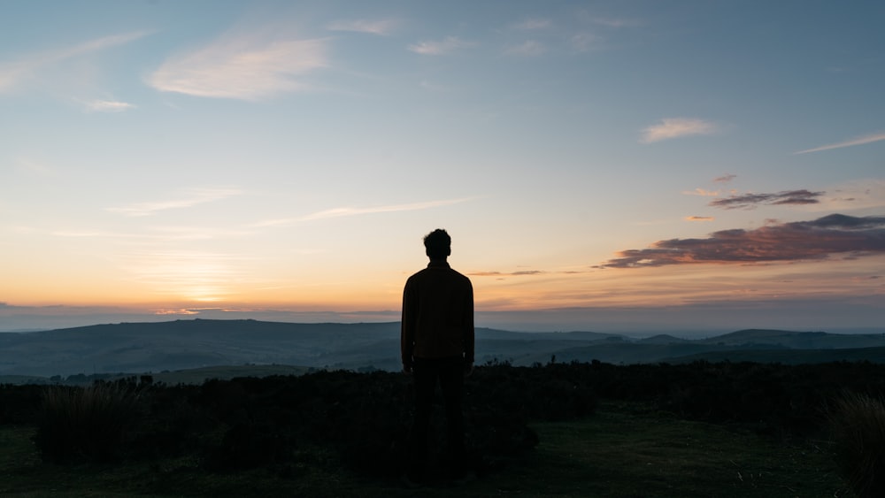 Silhouette eines Mannes, der bei Sonnenuntergang auf grünem Grasfeld steht