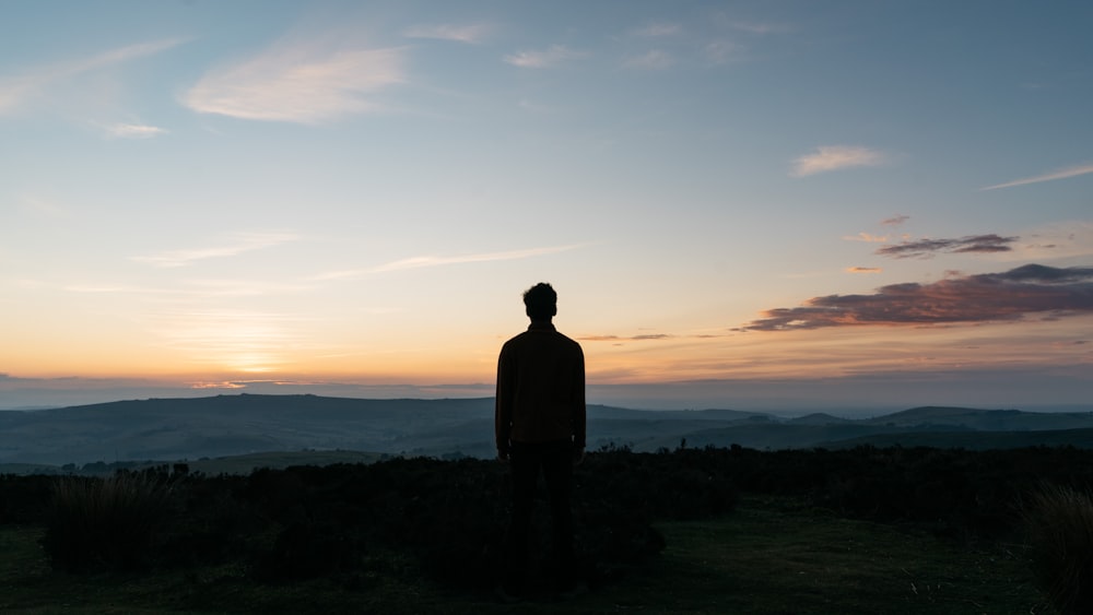 silhouette of man standing on green grass field during sunset