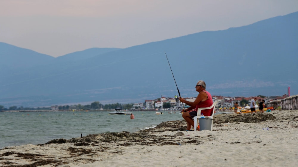 Hombre con camisa roja sentado en un barco blanco y azul en la playa durante el día