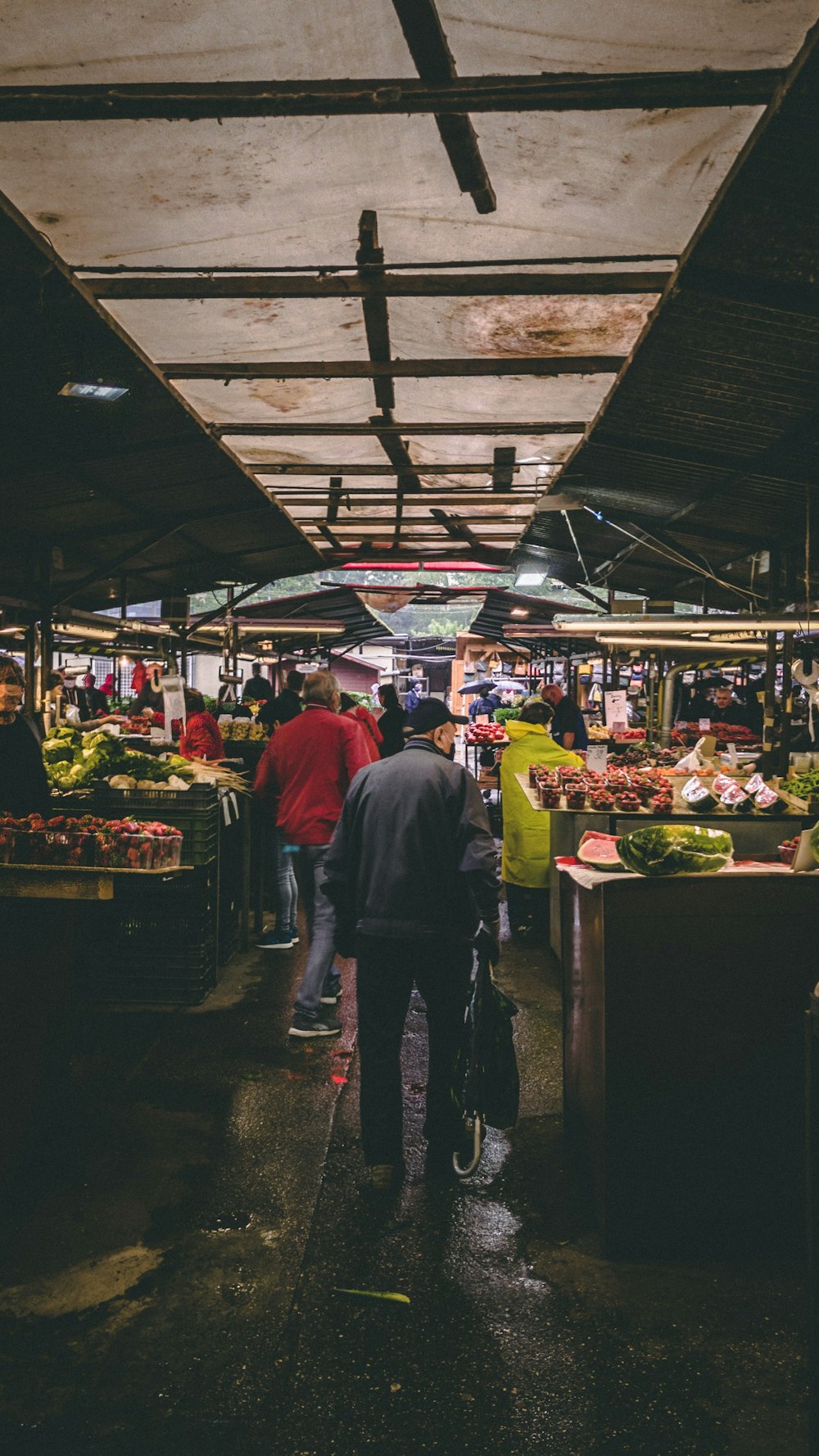 Homme en chemise grise à manches longues debout devant un stand de légumes