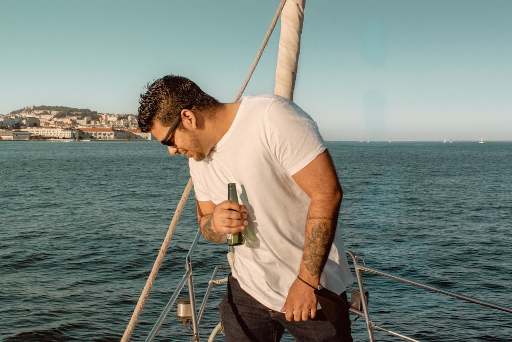 man in white crew neck t-shirt and black pants holding a glass of drink