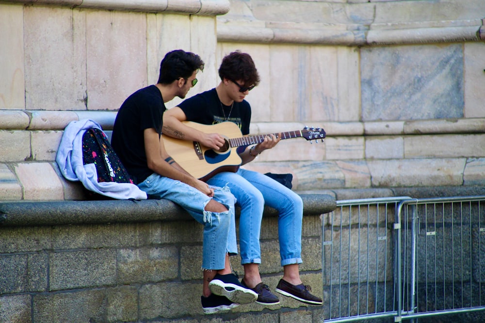man and woman sitting on concrete bench playing guitars