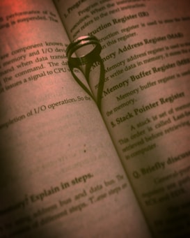 An open book with a ring placed between the pages, casting a heart-shaped shadow in the center. The text on the pages is focused on technical topics, possibly related to computer science or programming.