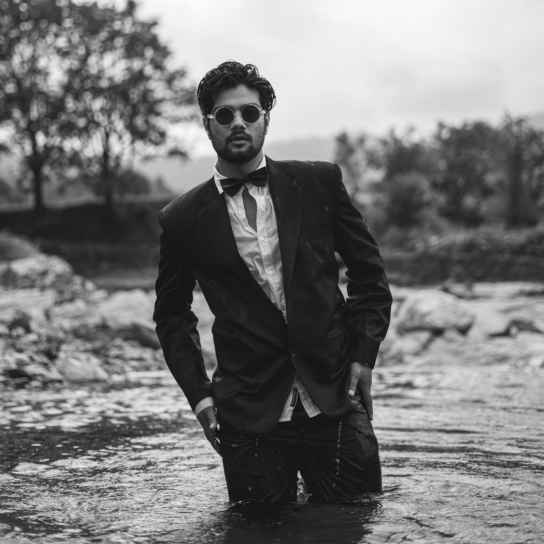 man in black suit jacket and black sunglasses standing on water
