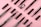 Several makeup brushes and eyebrow pencils are neatly arranged on a pink background. The items are in various states of assembly, with some showing bristles and others revealing the pencil tips.
