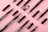 Several makeup brushes and eyebrow pencils are neatly arranged on a pink background. The items are in various states of assembly, with some showing bristles and others revealing the pencil tips.