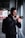 A person with glasses is holding a camera, preparing to take a photograph while standing in an urban setting. They are wearing a dark hoodie and carrying a backpack, suggesting they might be exploring or on a photographic assignment. The background shows an industrial or modern building environment, partially blurred.