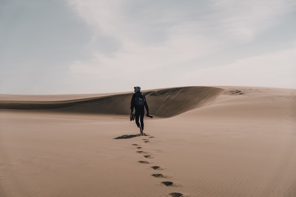 man in black jacket walking on brown sand during daytime