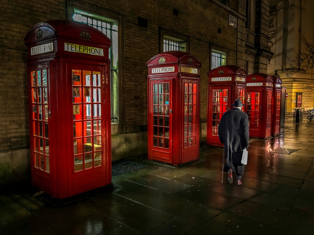 man in black coat standing beside red telephone booth