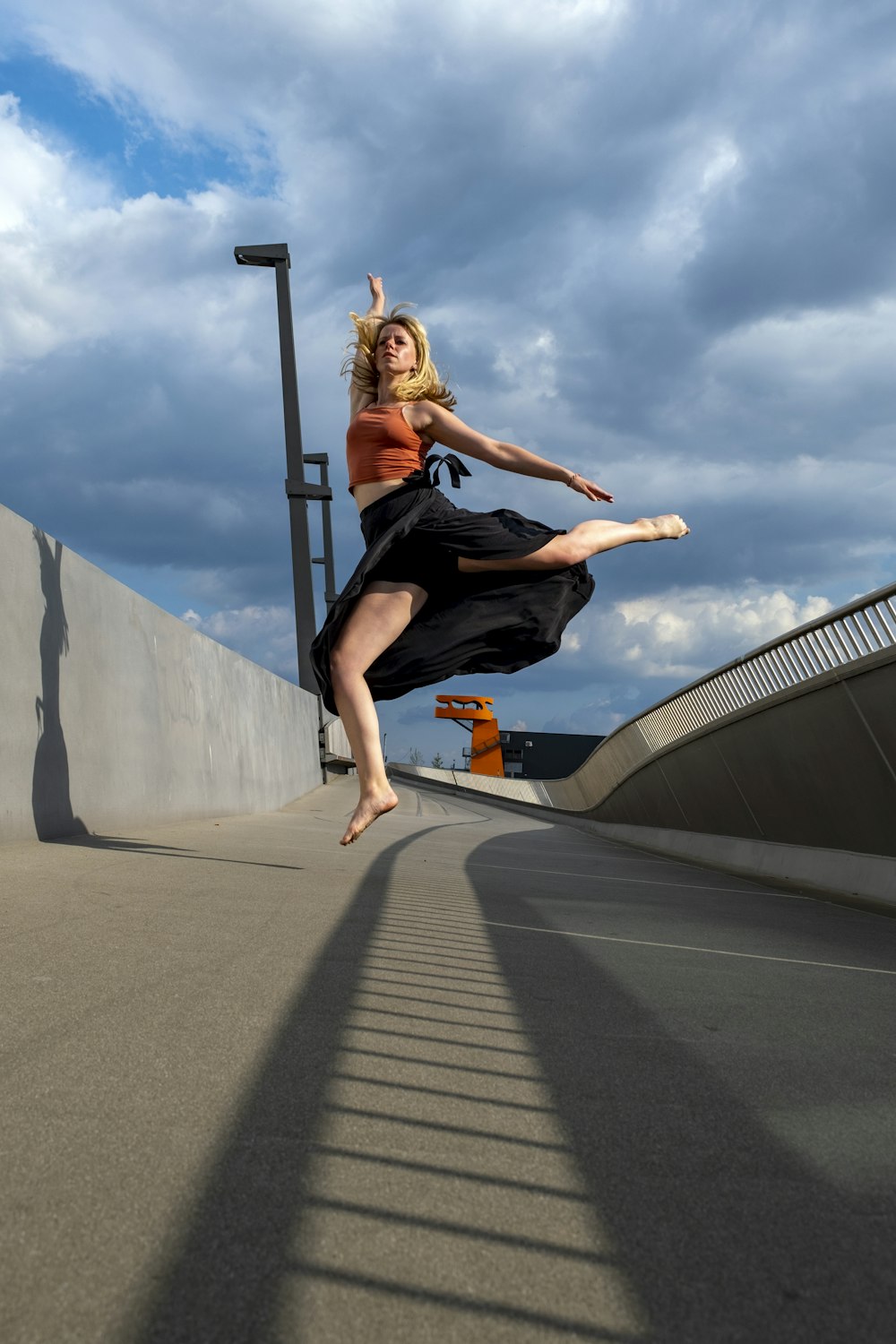 woman in black tank top and black pants jumping on gray concrete road during daytime