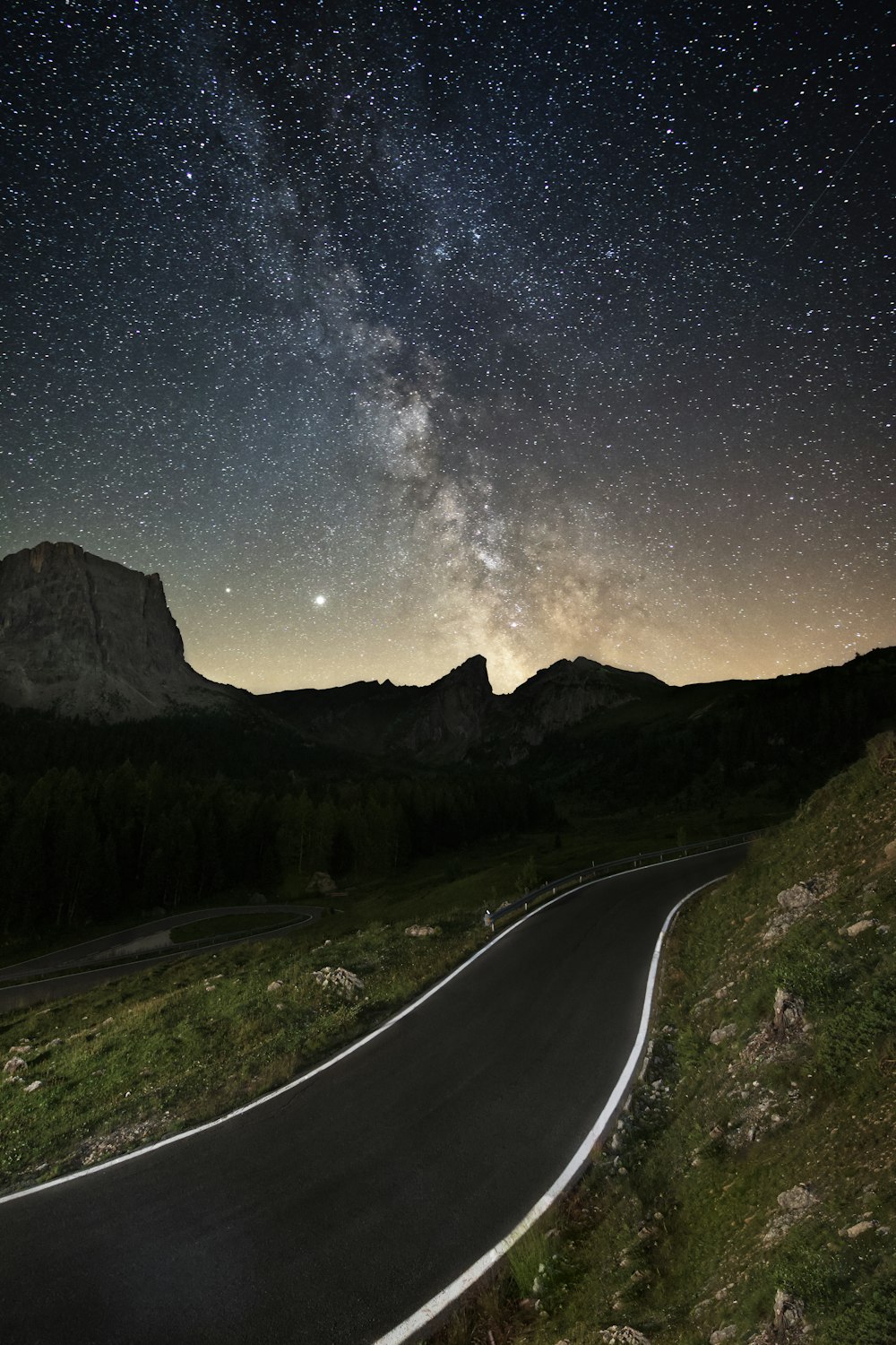 gray concrete road between green grass field during night time