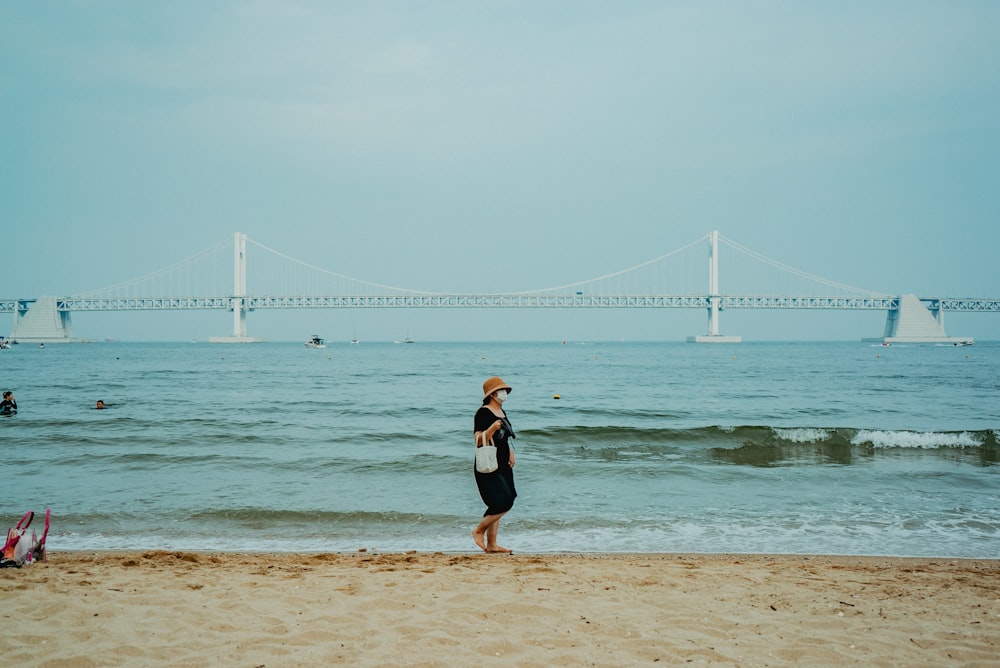 woman in black dress walking on beach during daytime