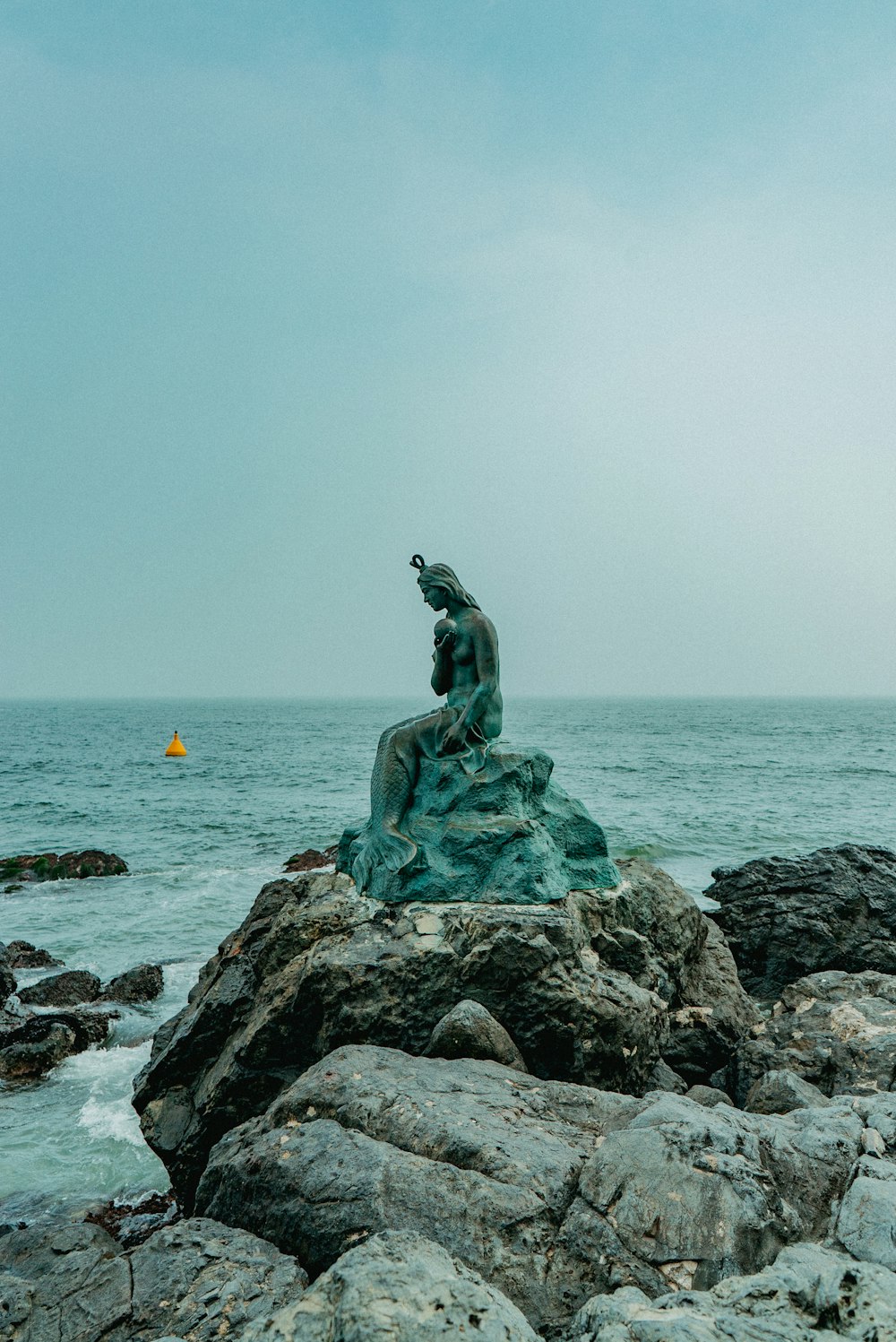 Estatua de una mujer en una roca cerca del océano
