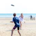 A smiling woman wearing a colorful solviva t-shirt at the beach, holding a frisbee with the ocean in the background.