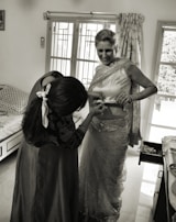 A caregiver gently assisting an older woman with adaptive clothing in a bright, cheerful room.