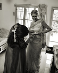 A friendly caregiver helping a smiling woman with dressing in a bright, welcoming room.