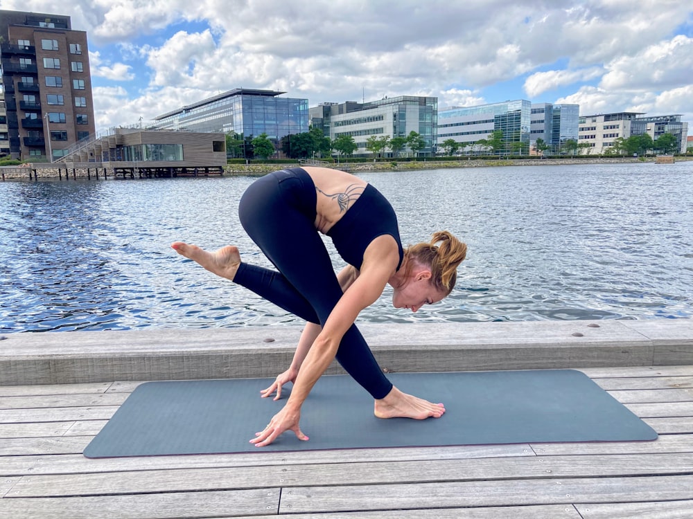 woman in blue tank top and blue leggings doing yoga near body of water during daytime
