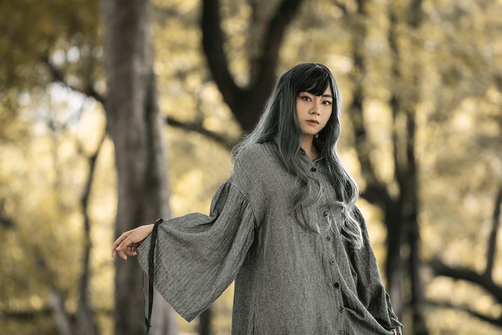 woman in gray long sleeve shirt standing near trees during daytime