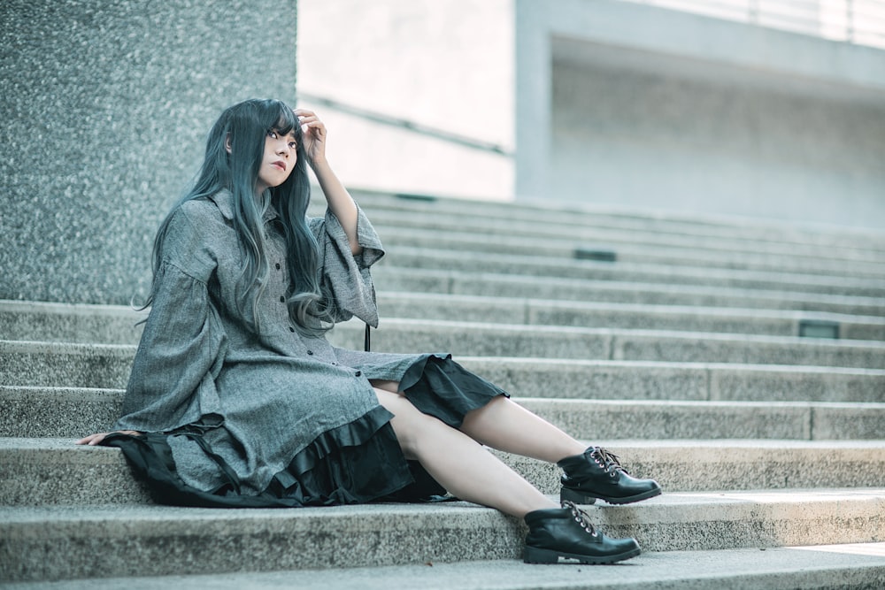 woman in gray long sleeve shirt and black skirt sitting on gray concrete stairs