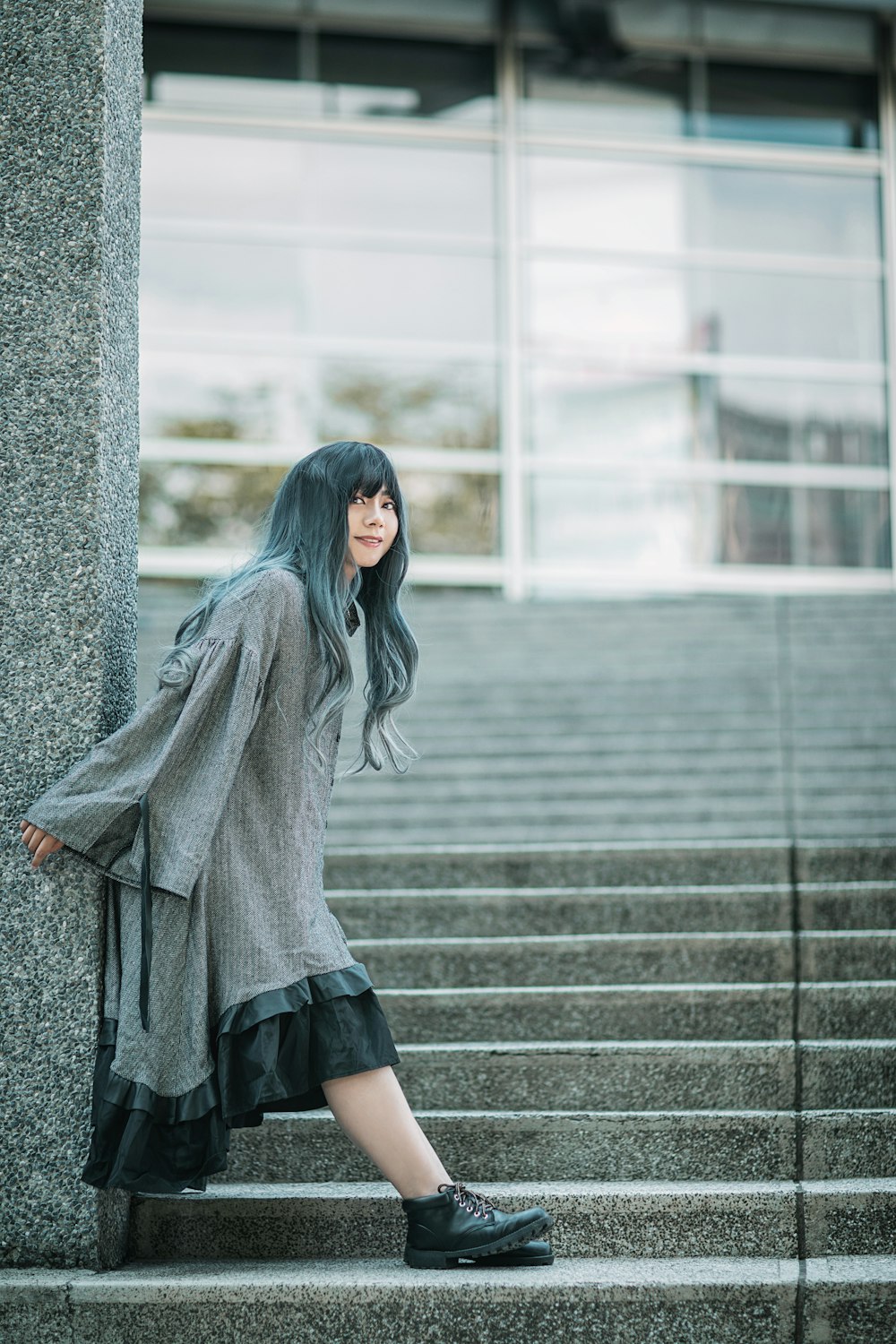 woman in gray sweater and black skirt standing on gray concrete stairs