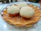 Three round, fluffy baked goods rest on an ornate, woven orange basket, placed on a marble countertop.