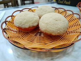 Three round, fluffy baked goods rest on an ornate, woven orange basket, placed on a marble countertop.