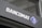 A modern sign with the word 'BANCOMAT' in bold, white letters is prominently displayed on a dark surface. To the right of the text is a blue and white logo resembling a stylized letter 'B' encased in a diamond shape.