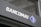 A modern sign with the word 'BANCOMAT' in bold, white letters is prominently displayed on a dark surface. To the right of the text is a blue and white logo resembling a stylized letter 'B' encased in a diamond shape.
