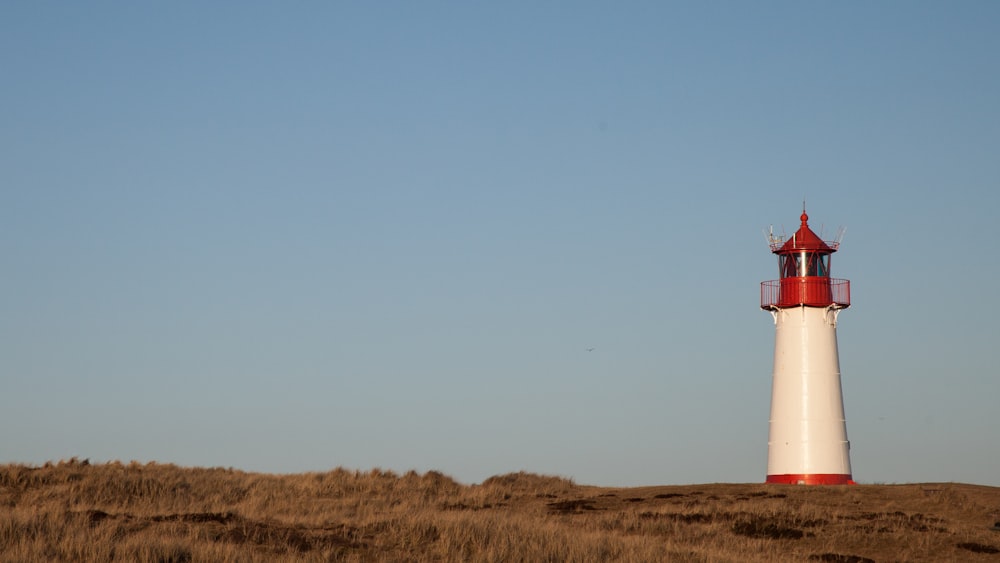 farol marrom e branco no campo de grama marrom sob o céu azul durante o dia