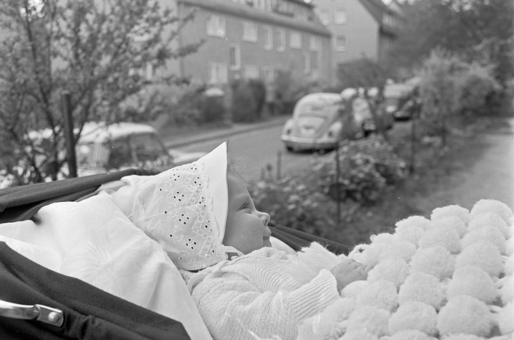 grayscale photo of baby lying on bed covered by white blanket