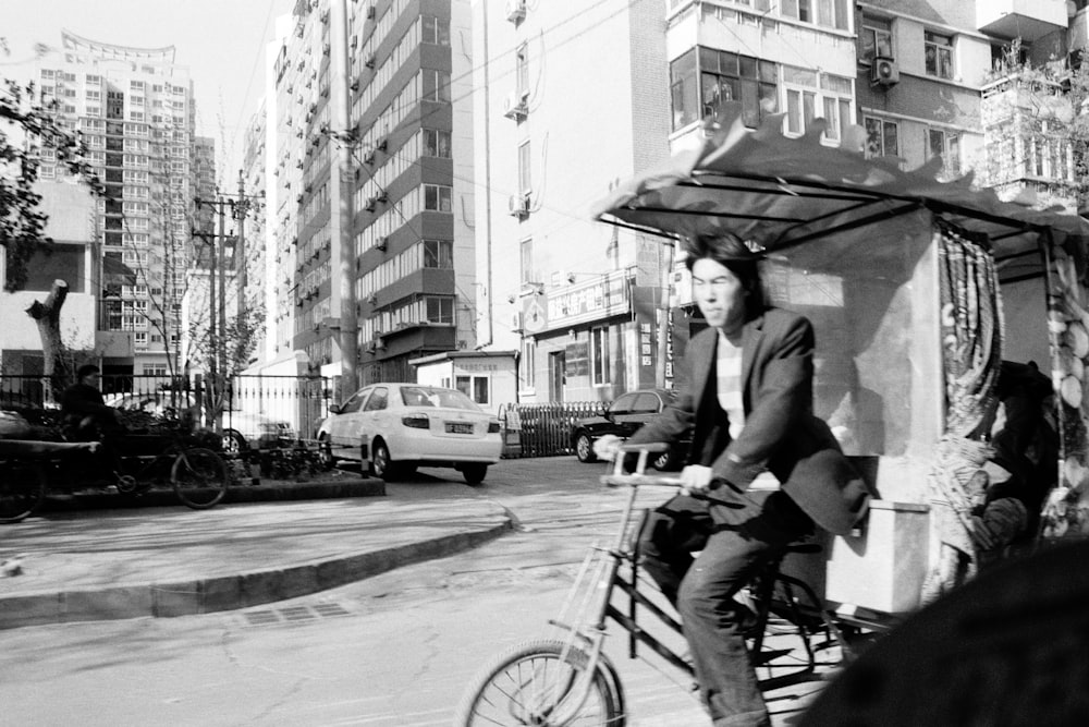 man in black jacket riding bicycle on street in grayscale photography