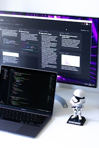 A friendly robot and a laptop displaying software code side by side in a bright workspace