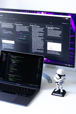 A clean, modern workspace with a laptop displaying code and a small 3D robot figurine beside it.