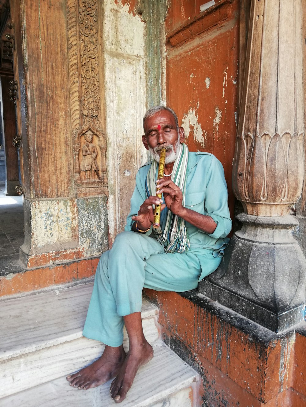 man in green thobe playing trumpet sitting on concrete bench