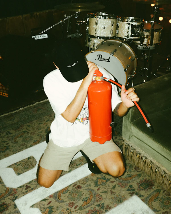 Someone kneeling by a drum kit holding a fire extinguisher