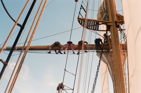 Crew members performing maintenance on a ship's deck under clear blue skies.