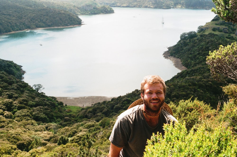 man in gray crew neck t-shirt standing on green grass field near body of water