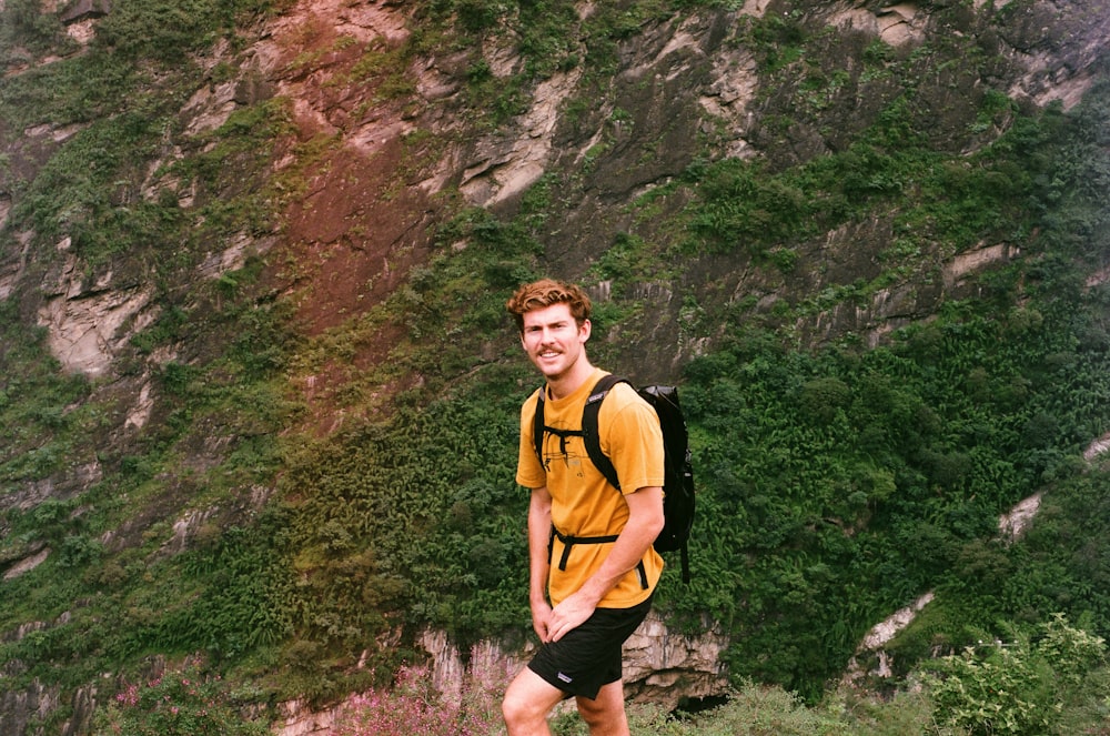 woman in yellow tank top and black shorts standing near rocky mountain during daytime