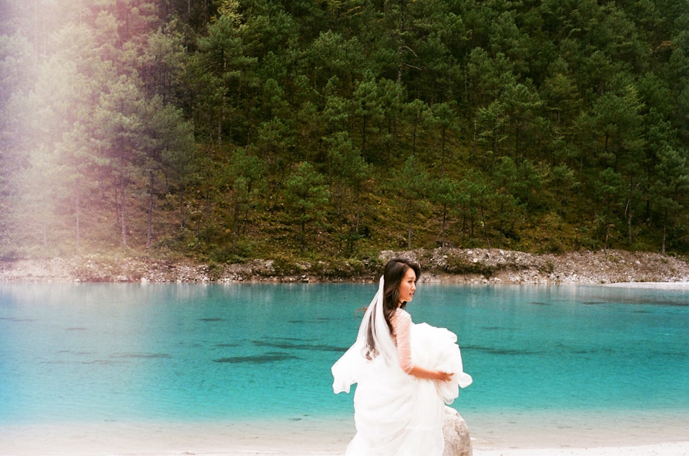 woman in white long sleeve dress standing on white sand near body of water during daytime